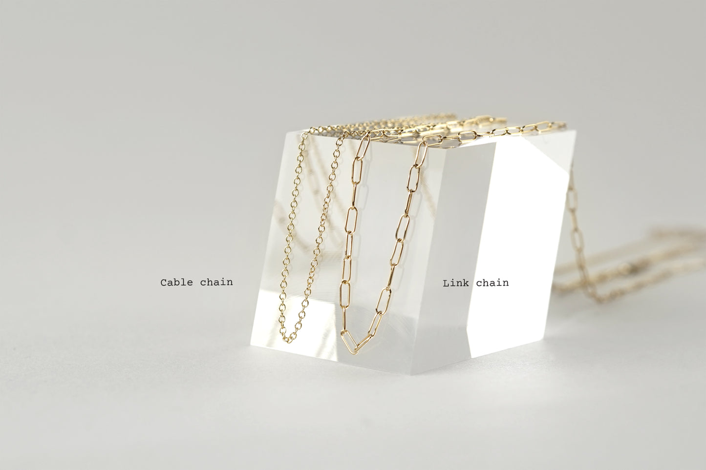 Two gold necklaces on a clear stand with 'Cable chain' and 'Link chain' labels on a light gray background.