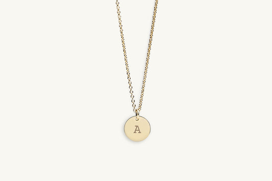 Gold necklace with a round pendant featuring the letter 'A' on a light beige background