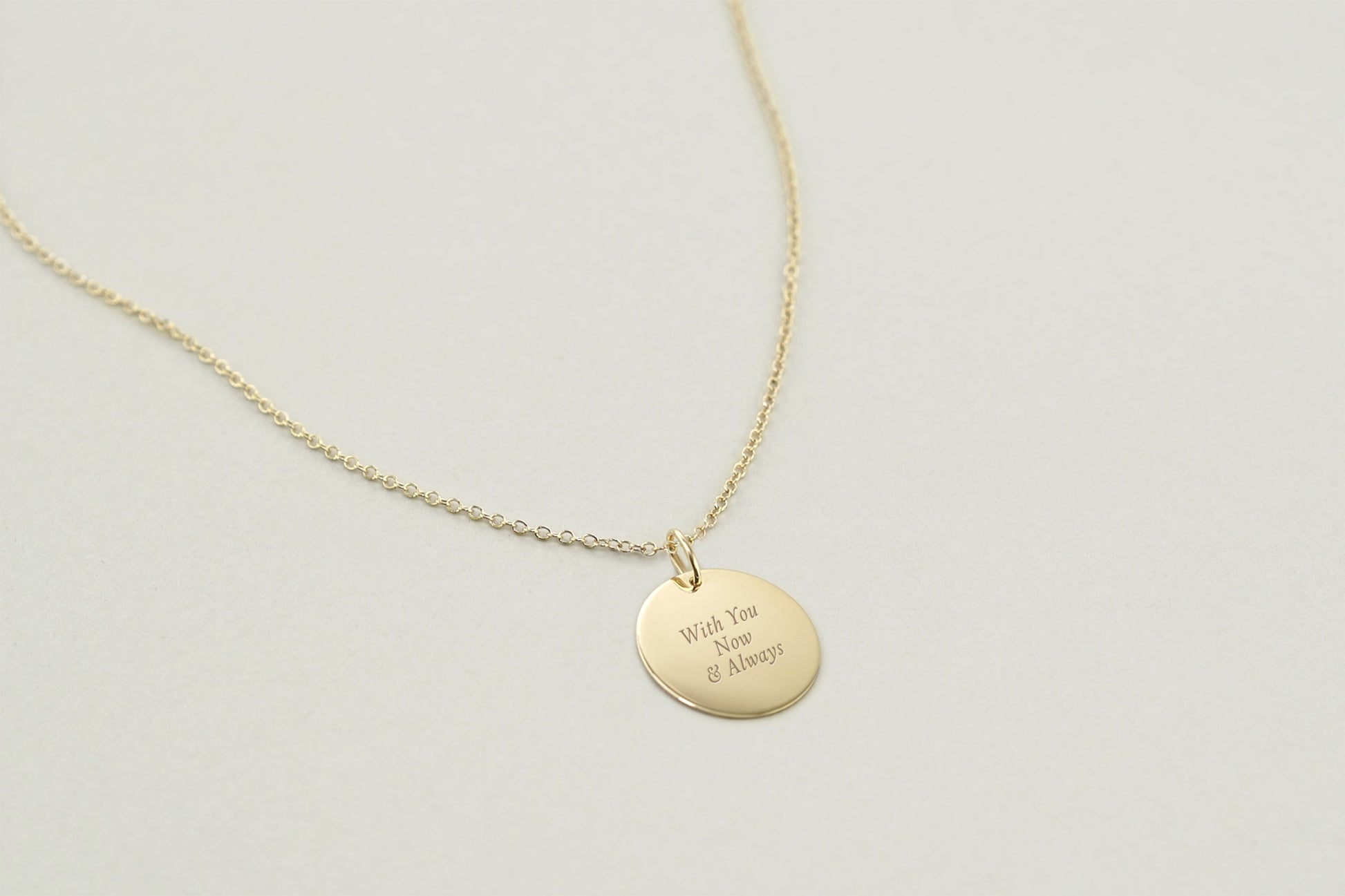 Gold necklace with a round pendant on a light gray background