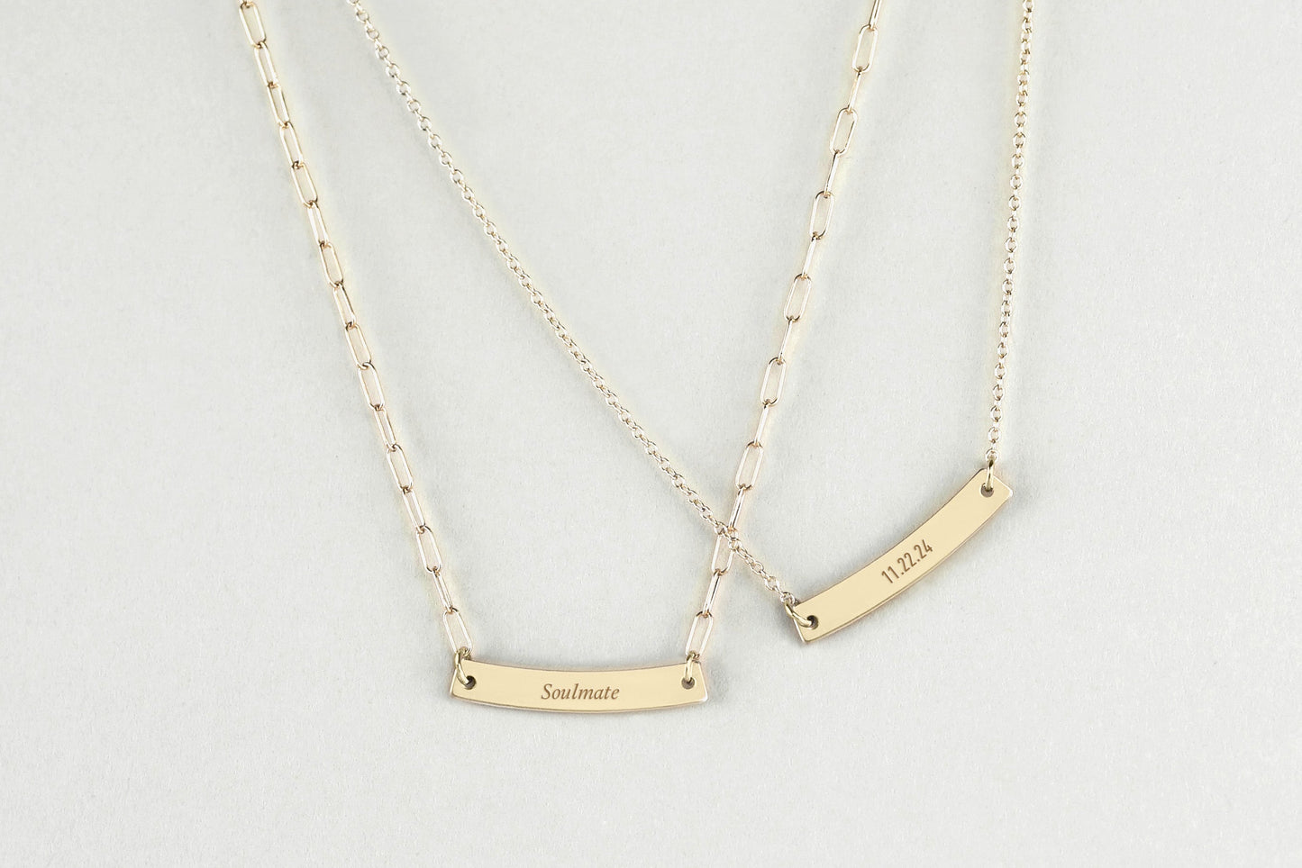 Two gold necklaces with personalized gold bar pendants on a light gray background