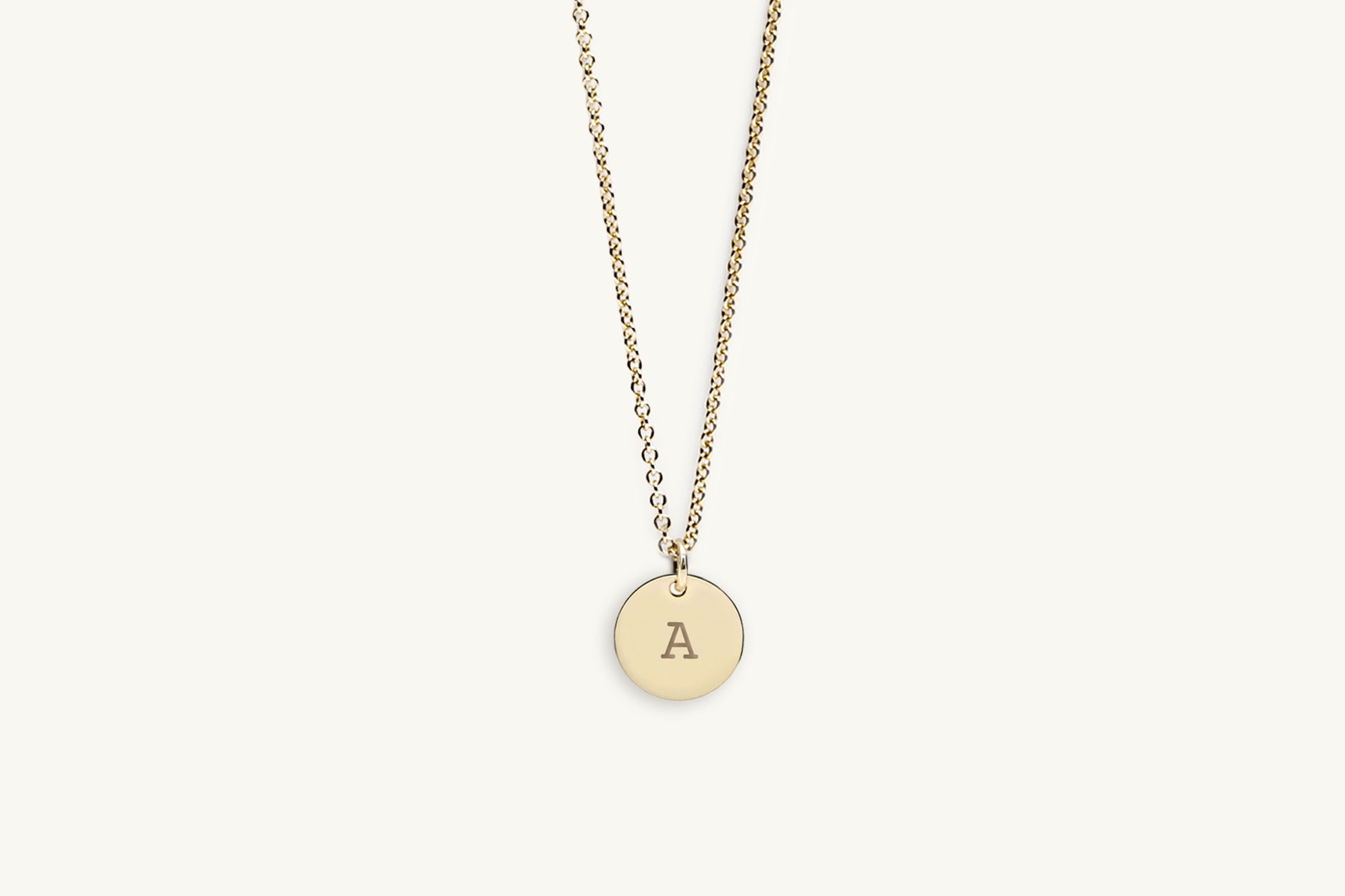 Gold necklace with a round pendant featuring the letter 'A' on a light beige background