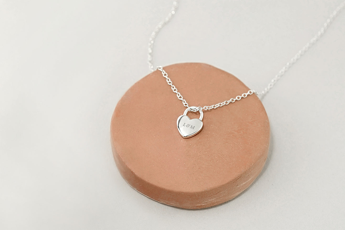 Silver necklace with a heart-shaped pendant on a ceramic stand