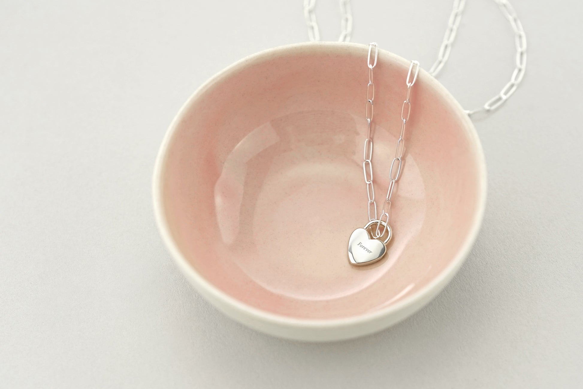 Necklace with a heart pendant on a pink dish against a light gray background