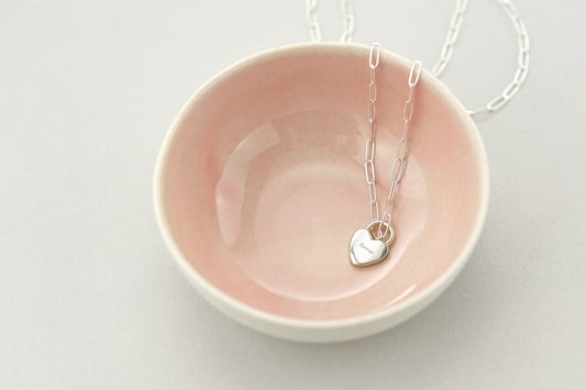 Necklace with a heart pendant on a pink dish against a light gray background