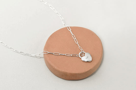 Silver necklace with a heart-shaped pendant on a ceramic stand against a white background