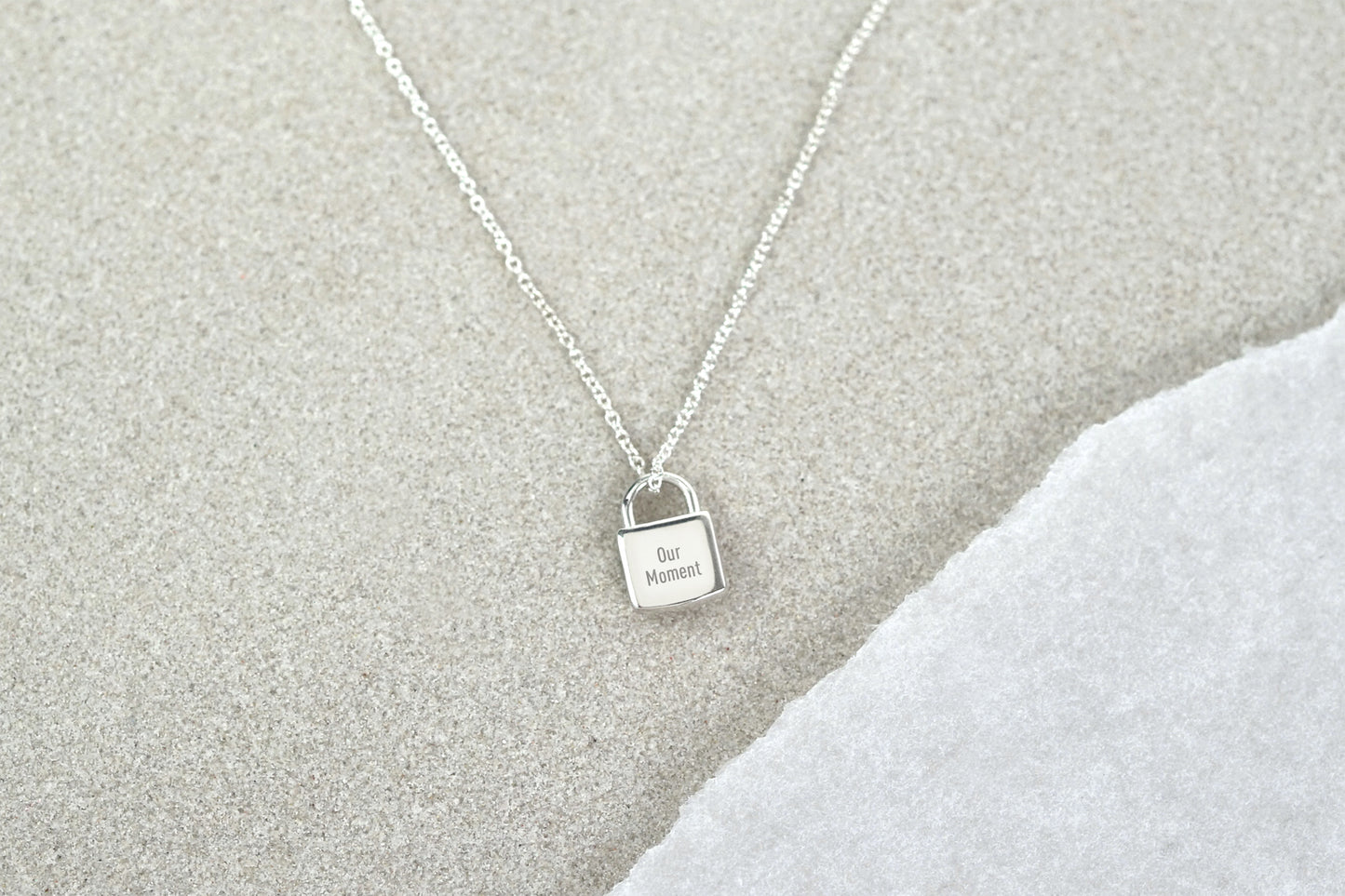 Silver necklace with a lock-shaped pendant on a textured gray surface