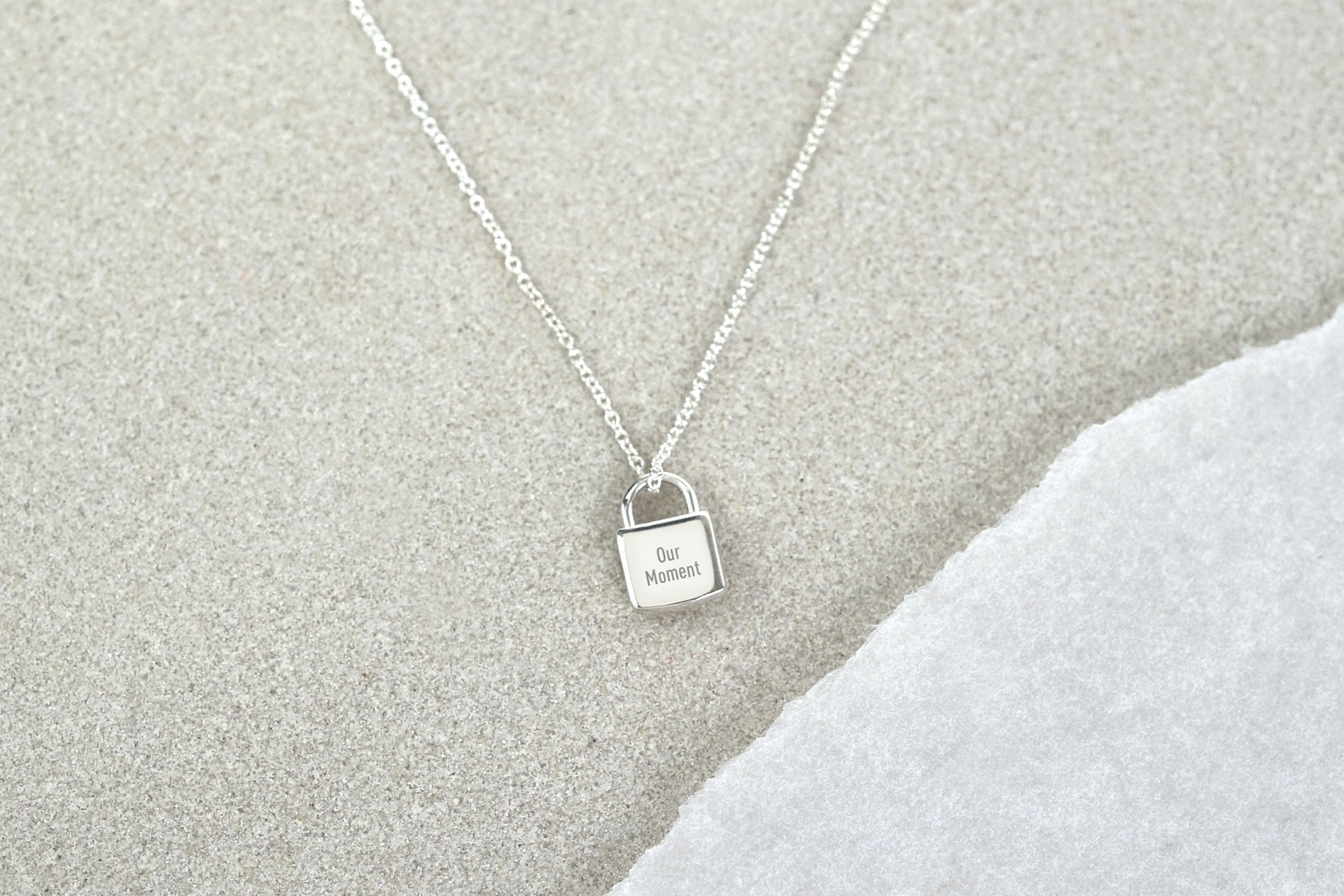 Silver necklace with a lock-shaped pendant on a textured gray surface