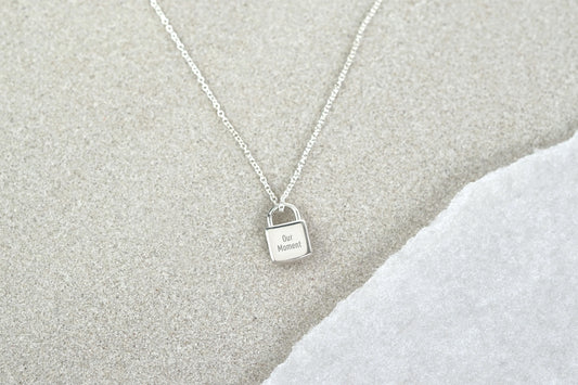 Silver necklace with a lock-shaped pendant on a textured gray surface